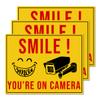 GOLEEX Pack 4 Pcs Smile You're On Camera Stickers Security Notice Bumper Sticker Outdoor Window Automotive Exterior Decal Reflective Video Surveillance Label for House Decoration view 1